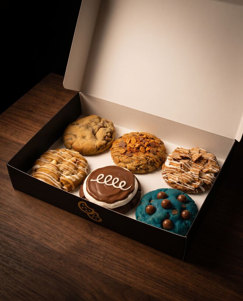 An open black Crave box of six full-size cookies on a dark table